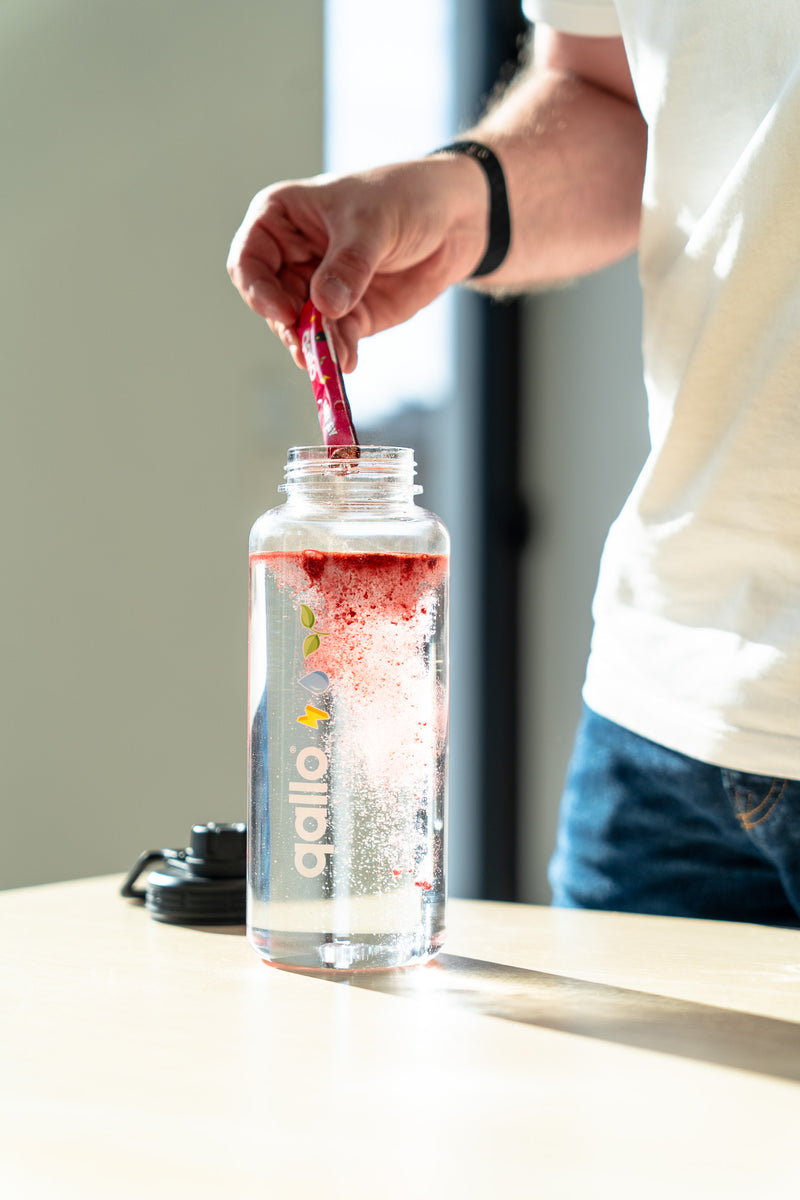 Een zakje Qallo wordt in een drinkfles gegoten