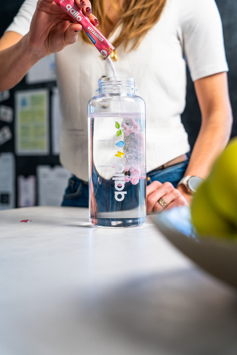 Een zakje Qallo Vitamins Raspberry wordt in een drinkfles gegoten